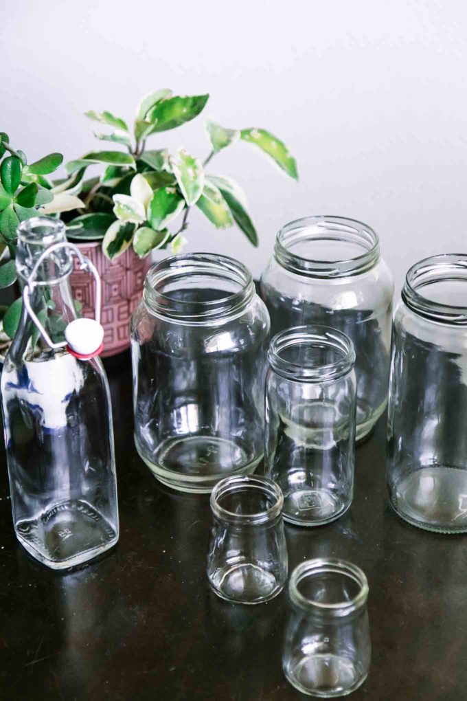 empty glass food jars without labels on a wooden table with a green plant in the background