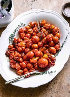 burst cherry tomatoes on a white plate with a gold fork on a wood table