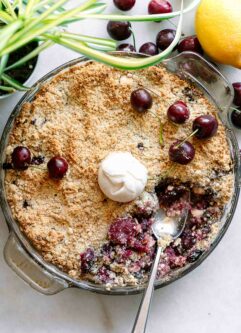 a round baking dish with a baked cherry crisp and a scoop of ice cream on top with a gold fork