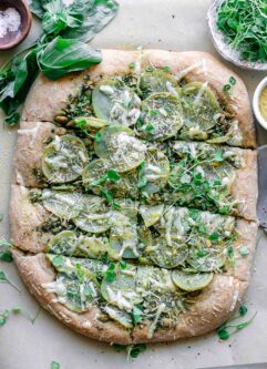 plant-based pesto pizza with potatoes on a white table with fresh basil leaves